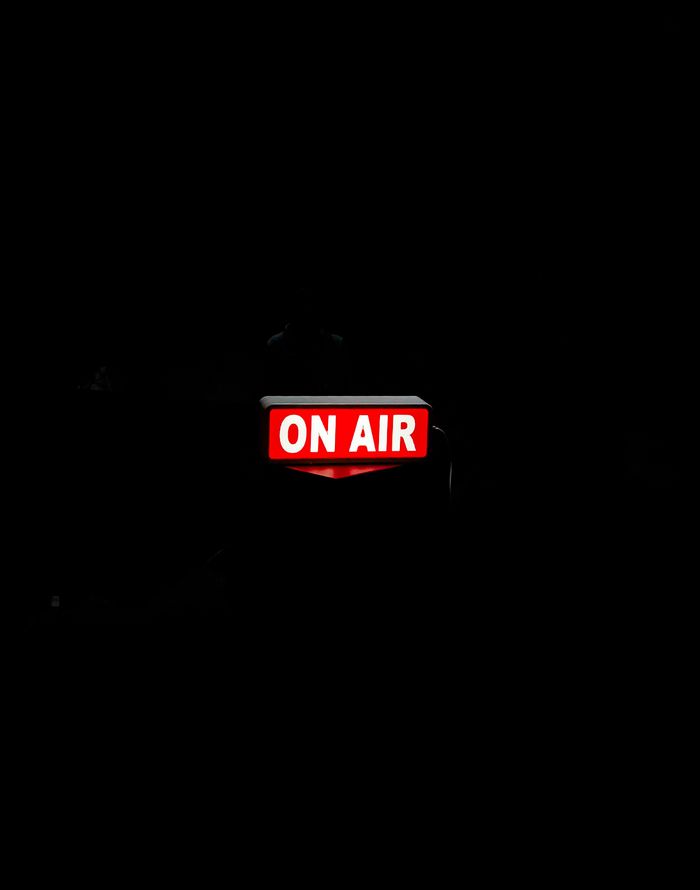 Bright 'On Air' sign glows in dark studio, creating moody atmosphere.