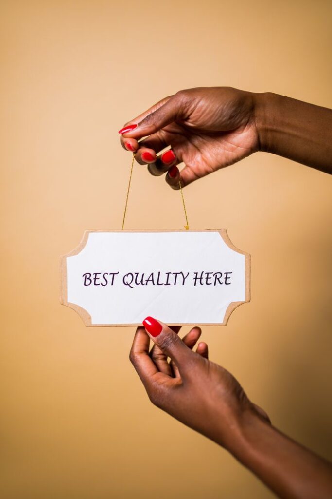 Stylish female hands with red nails holding a sign that says 'Best Quality Here' against a soft background.